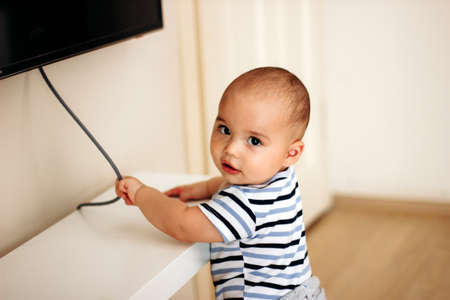Sweet naughty baby boy pulls the electric cord from TVの写真素材