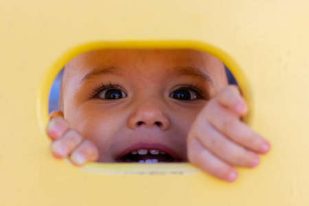 Cute little baby boy playing at children playground. Child looking to camera from yellow holeの写真素材