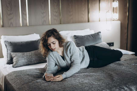 Happy smiling teenager girl watching video on her phone. Online chat with friends. girl lying on the...