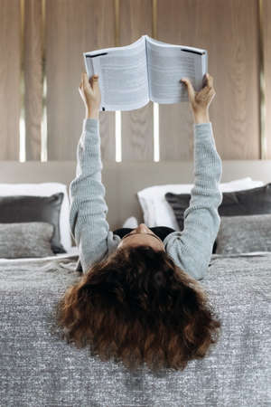 Teenager girl with curly hair lying on bed and reading book