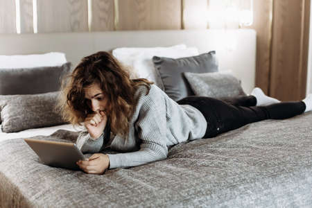 Teenager girl watching video on tablet lying on the bedの写真素材