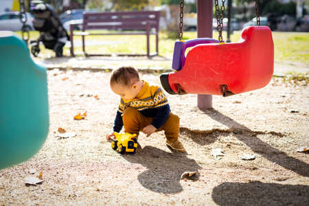 Funny baby boy playing outdoors playground. Toddler plays with toy car. Sunny dayの写真素材