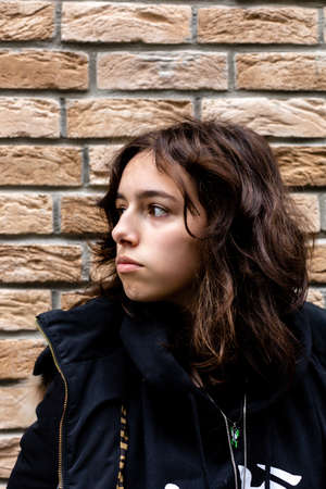 Portrait of teenager girl in front of bricks wall. Black wearing teen looking side