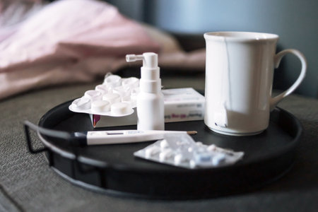Medicines for seasonal colds. Nasal spray, thermometer and pills on a black tray in the bed.