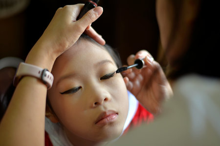Family activities A mother grooming her daughter with mascara on her eyelashes in her bedroom at...