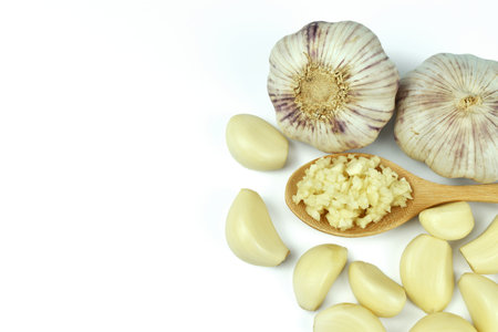 Chopped garlic in wooden spoon surrounded by peeled garlic cloves ready for cooking on a white background with copy spaceの写真素材