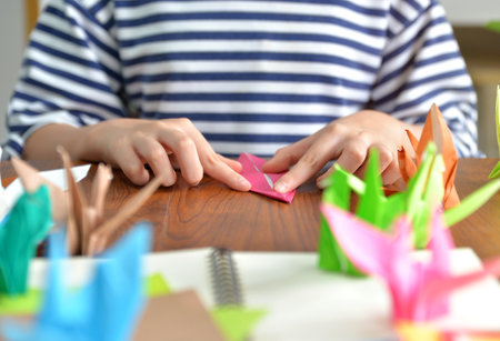 Female hands folding paper birds colorful as a hobby on a wooden table at homeの写真素材