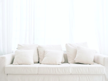 Plain white sofa in living room Decorated with white fabric pillows Behind it is a translucent curtain. Natural light shines through and makes it bright and clean.の写真素材