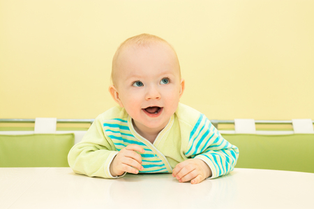 happy little baby sits at table and smiles. beautiful small child boy cheerful looking and laughsの写真素材