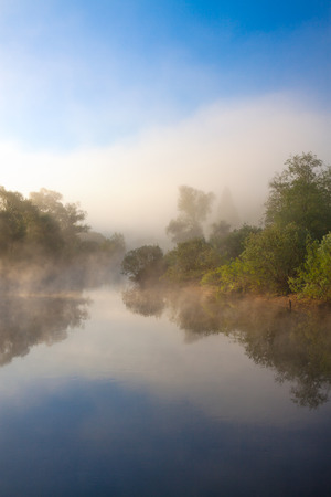 summer rural landscape with river, fog and forest at sunriseの写真素材