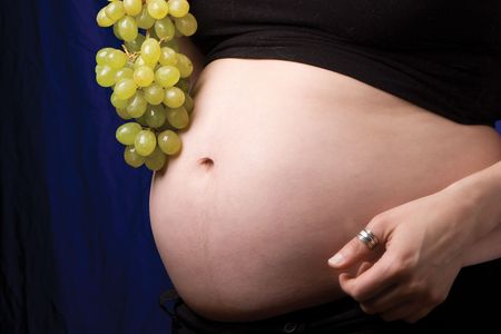 Close up of a pregnant belly with grapes near the belly button