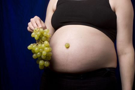 Pregnant women holding a green grapes to her bellyの写真素材