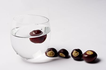 Glass cup filled with water containing one chest nut, four chest nut are on the side waiting to get their turn to dipの写真素材