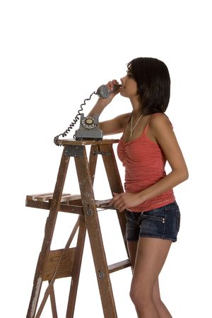 teenage girl standing on ladder talking on a old rotary phoneの写真素材