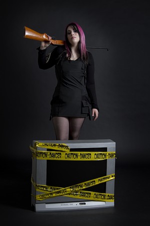 women with rifle on her shoulder standing behind a television with yellow danger tap on itの写真素材