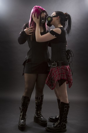 two teenage girls wearing goth inspired clothes with pink, black hair and gas mask, trying to kissの写真素材