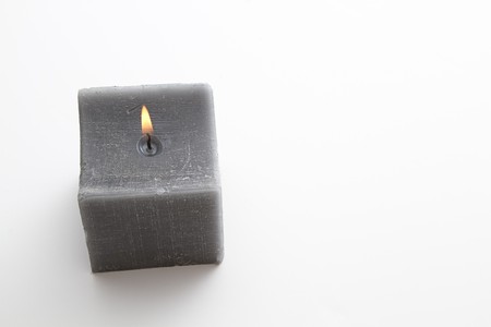 lit square gray candle against white backgroundの写真素材