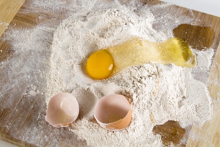cracked chicken egg flowing in a nest of flour with left over brown shellの写真素材