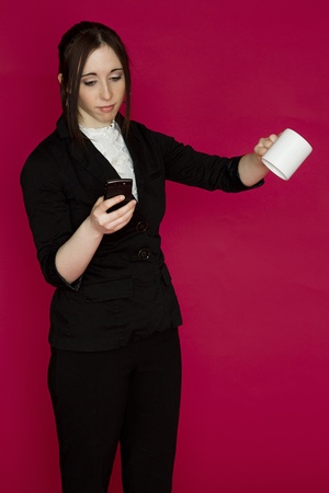 Young business woman flipping her cup of coffee and working off her smart phone against pink backgroundの写真素材