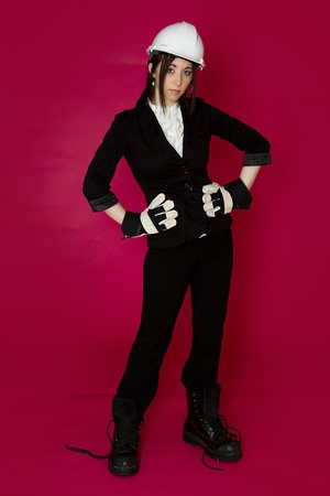 Young woman wearing white hard hat, construction glove and boots that are to big for her against a pink backgroundの写真素材