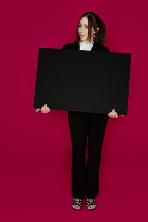 Young business woman wearing a business suit standing behind a black board against pink backgroundの写真素材