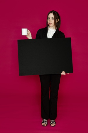 Young business woman holding a black board and a coffee cup with an inquiring expression against pink backgroundの写真素材