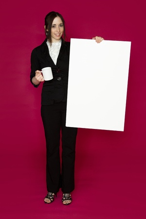 Young business woman holding a white board and a coffee cup against pink backgroundの写真素材