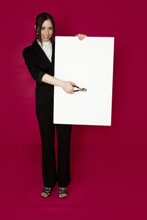 Young business woman holding a pair of plier pointing to a white board  against pink backgroundの写真素材