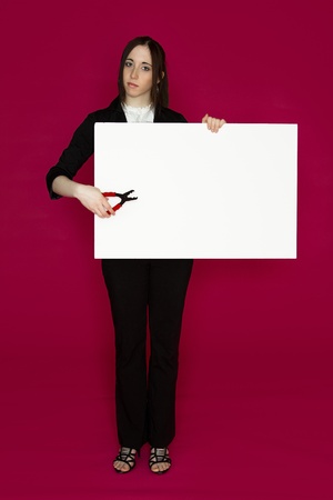 Young business woman holding a pair of pliers pointing to a white board  against pink backgroundの写真素材