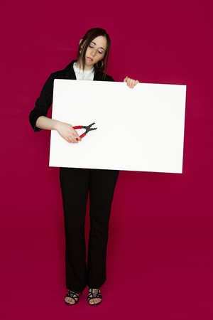 Young business woman holding a pair of pliers pointing to a white board against pink backgroundの写真素材