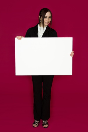 Smiling young business woman wearing a business suit standing behind looking down at a white board against pink backgroundの写真素材