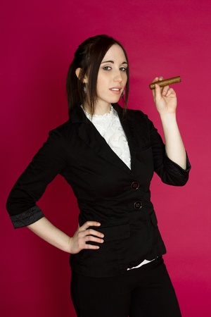 Young woman in a business suit smoking a cigar against a pink backgroundの写真素材