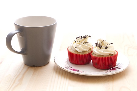 two vanilla frosted cupcake with chocolat cookie crumbs on an old fashion plate with a coffee cupの写真素材