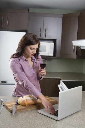Young woman with a glass of wine and a house bread that has been cut, working on a laptopの写真素材