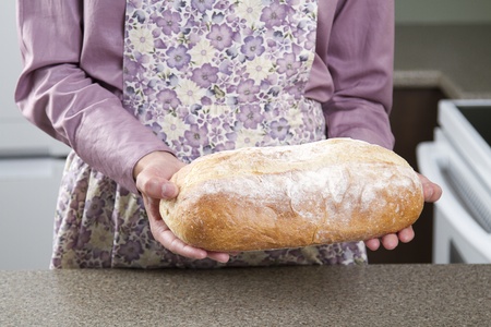 Woman wearing a apron holding a loaf of breadの写真素材