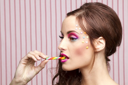 Young woman with colorful makeup and star candy glued to her face, bitting a candy caneの写真素材