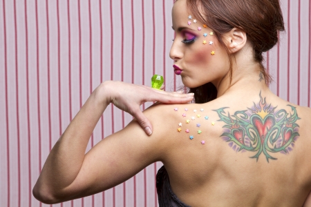 Young woman with colorful makeup and star candy glued to her face and body, kissing a lollipop ringの写真素材