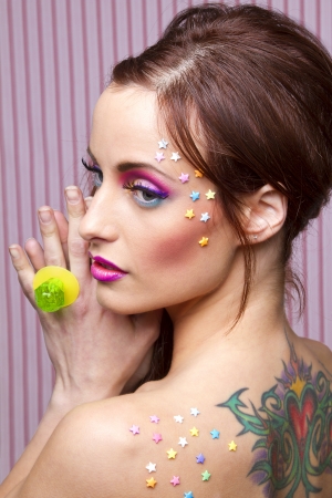 Young woman with colorful makeup and star candy glued to her face, showing a lollipop ringの写真素材