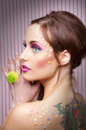 Young woman with colorful makeup and star candy glued to her face and a lollipop ringの写真素材