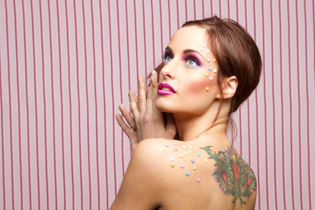 Young woman with colorful makeup and star candy glued to her face and back, looking upの写真素材