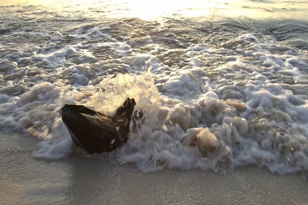 piece of wood sticking out of the sand being hit by wavesの写真素材