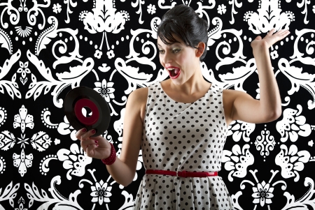 young woman in front of a black and white textured background with 60's inspired style, holding a small record with a red labelの写真素材