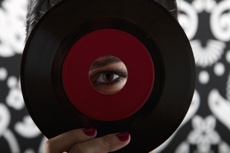 young woman looking through the hole of a small record with a red labelの写真素材