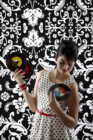 young woman in front of a black and white textured background with 60's inspired style, holding three small record choosing one to playの写真素材