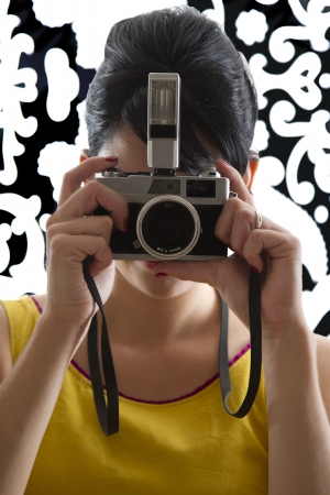 young woman in front of a black and white textured background with 60's inspired style, holding a SLR 35mm film cameraの写真素材