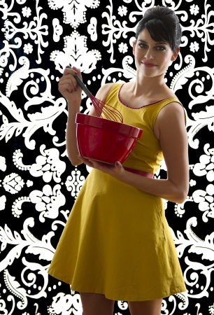 young woman in front of a black and white textured background with 60's inspired style, holding a red whisk in a red bowlの写真素材