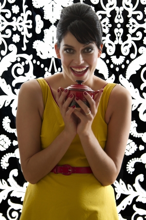 young woman in front of a black and white textured background with 60's inspired style, holding a red miniature crockpotの写真素材