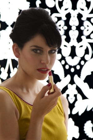 young woman in front of a black and white textured background with 60's inspired style putting on lipstickの写真素材