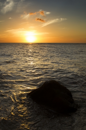 sunset over the calm pacific ocean warming a boulderの写真素材