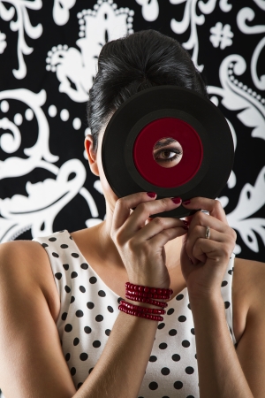 young woman looking through the hole of a small dusty record with a red labelの写真素材